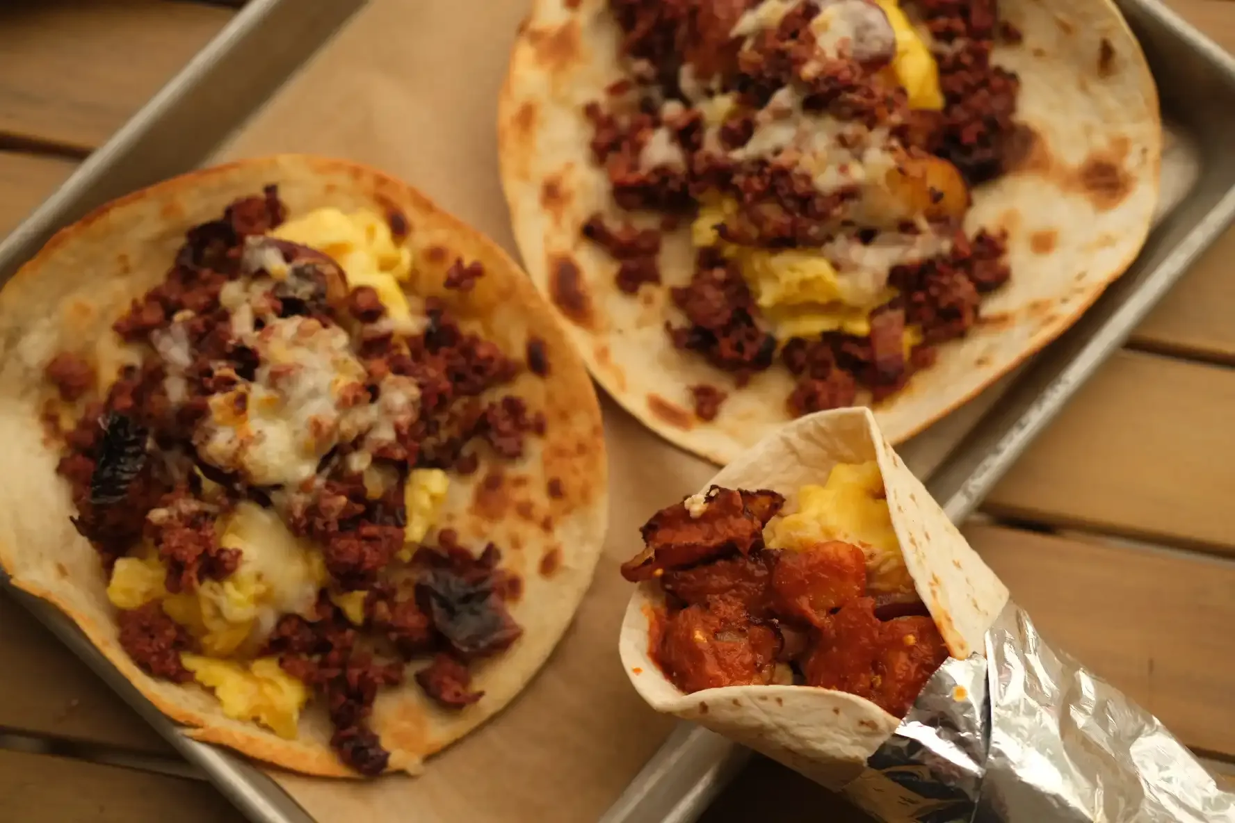 Chorizo, scrambled egg and melted cheese on griddled flour tortillas, with a foil-wrapped taco beside them